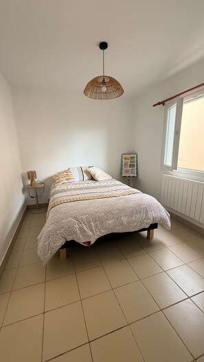 Une chambre à coucher avec un lit, un luminaire suspendu, une petite table avec une lampe et une fenêtre donnant sur un beau paysage.