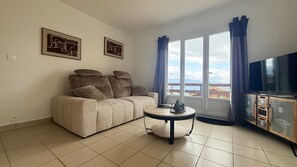 Una sala de estar con sofá, mesa de centro, televisor y ventana con cortinas.