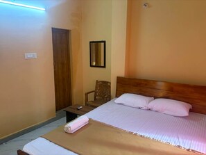 Un dormitorio con cama, una silla, una mesita de noche y un espejo fijado a la pared.