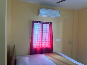 Una habitación con una cama, un equipo de aire acondicionado instalado en la pared y una ventana con cortinas rojas.