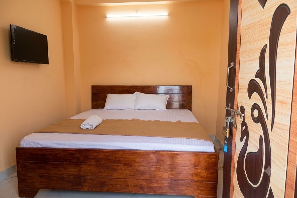 Una cama bien hecha con ropa blanca y un cabecero marrón en una habitación con una puerta de madera y un televisor de pantalla plana montado en la pared.