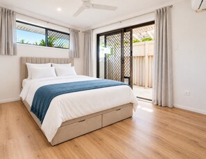Une chambre avec un lit, un ventilateur de plafond et une vue sur l’extérieur, accessible par une porte-fenêtre coulissante qui donne sur un espace extérieur.