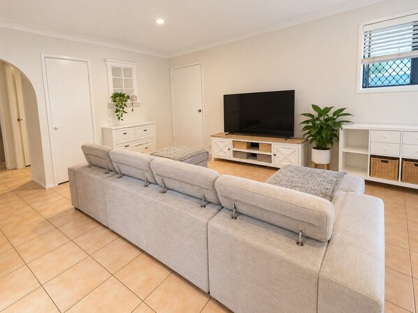 Un salon moderne doté d’un grand canapé en forme de L, d’un téléviseur à écran plat et d’une console blanche avec des rangements.