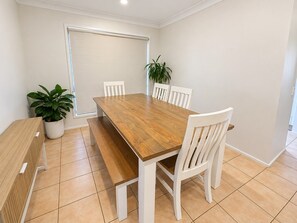Un coin repas avec une table en bois et des chaises blanches, une plante en pot et une vue sur l’extérieur.