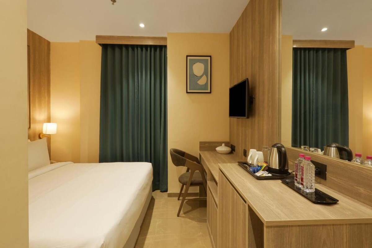 A hotel room with a bed, a desk, a chair, a television, and a mirror.