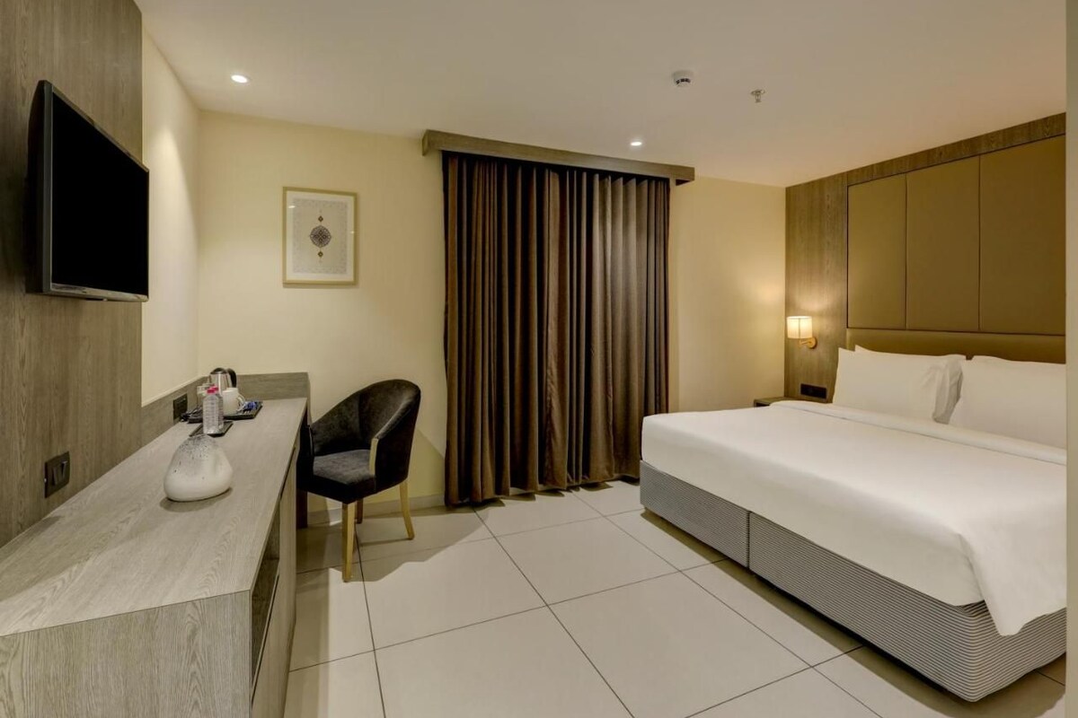 A hotel room with a bed, a desk, a chair, a television, and a window with curtains.