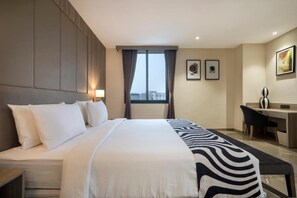 A hotel room with a large bed, a desk, and a window with curtains. - POP 84978J Sunday Vadodara Palace Hotel (Vadodara)