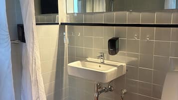 A bathroom with a white sink, a mirror, a shower curtain, and a toilet.