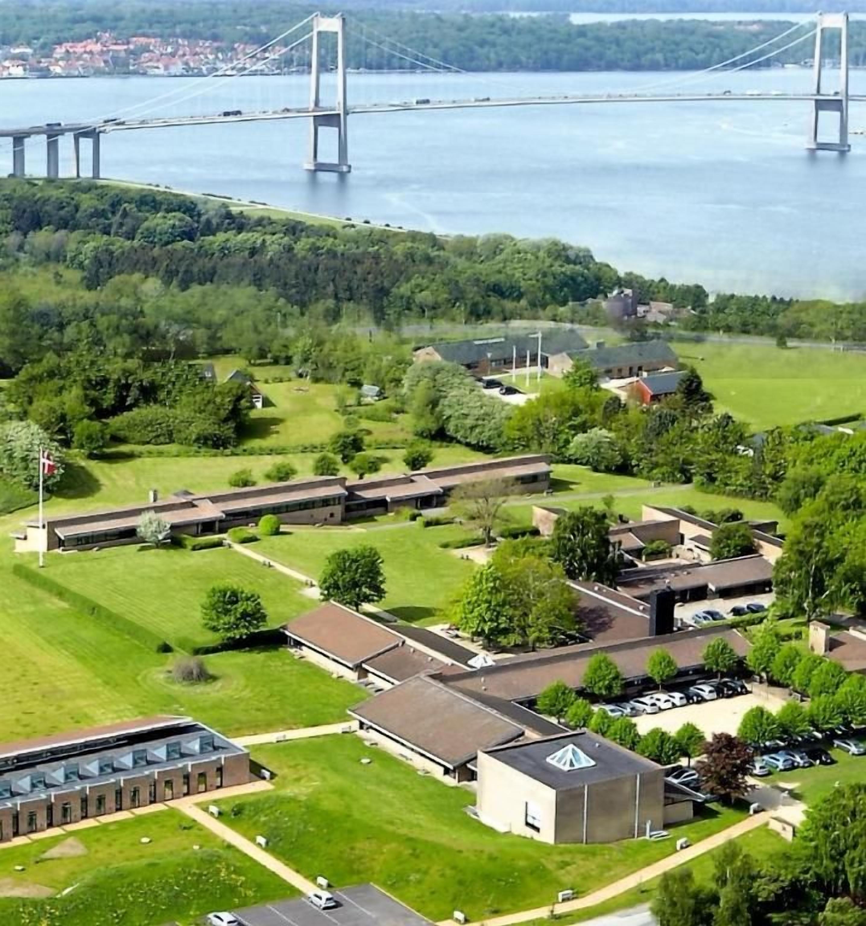 An aerial view of a campus with buildings, parking, and a bridge in the background.