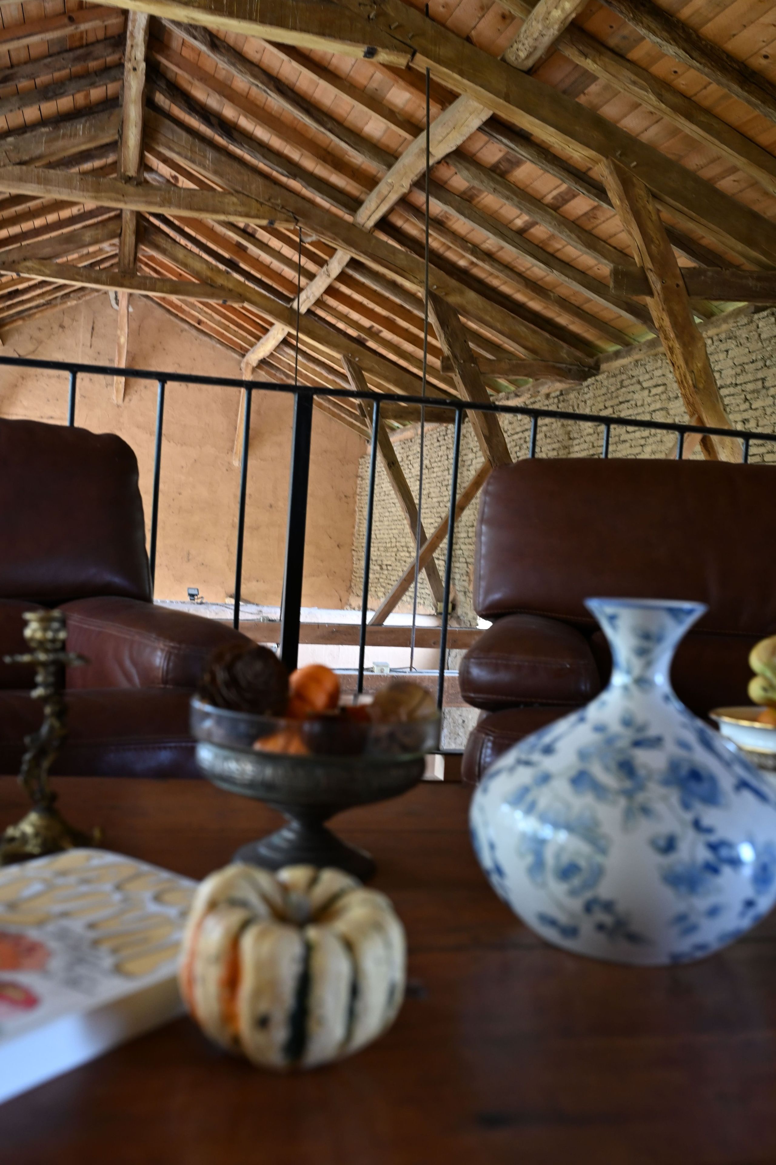 Un interior rústico con un alto techo de madera, un sofá de cuero, una mesa de comedor con un jarrón y una decoración de calabaza, y una pared de ladrillo.