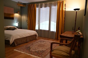 Une chambre à coucher avec un lit, une chaise, une table, une lampe et une fenêtre avec des rideaux.