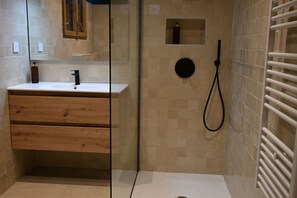 Une salle de bain avec un meuble-lavabo en bois, un miroir, une douche avec un pommeau de douche amovible et un porte-serviettes.