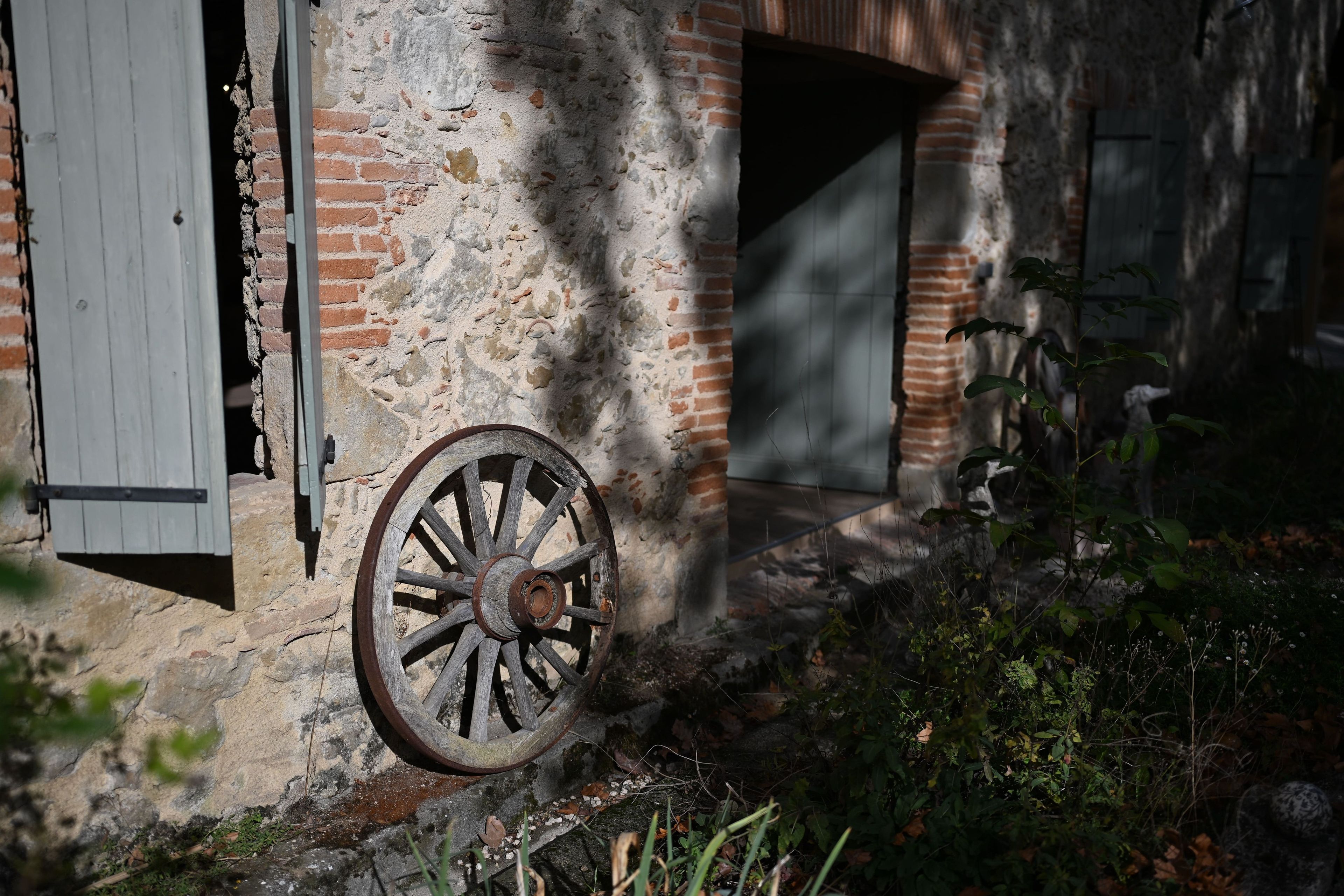Un edificio antiguo con una rueda de madera desgastada, un muro de ladrillo y una puerta entreabierta.