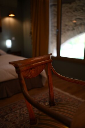 Une chaise en bois dans une pièce faiblement éclairée, avec un lit et une fenêtre en arrière-plan.