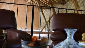Un interior rústico con un alto techo de madera, un sofá de cuero, una mesa de comedor con un jarrón y una decoración de calabaza, y una pared de ladrillo.