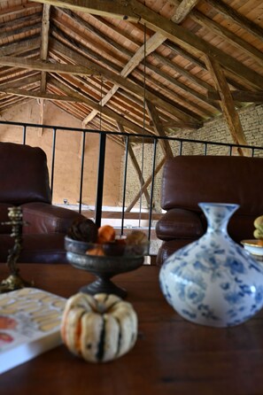 Un intérieur rustique avec un haut plafond en bois, un canapé en cuir, une table à manger agrémentée d’un vase et d’une citrouille en guise de centre de table, et un mur en briques.