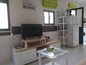 Un saló modern amb televisió de pantalla plana, màquina de cafè, rentadora i zona de menjador amb taula de vidre.