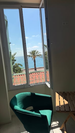 A room with a large window overlooking a beach, a green chair, and a wooden bench. - Room with Private Bathroom and Air Conditioning – Cagnes-sur-Mer (Cagnes-sur-Mer)