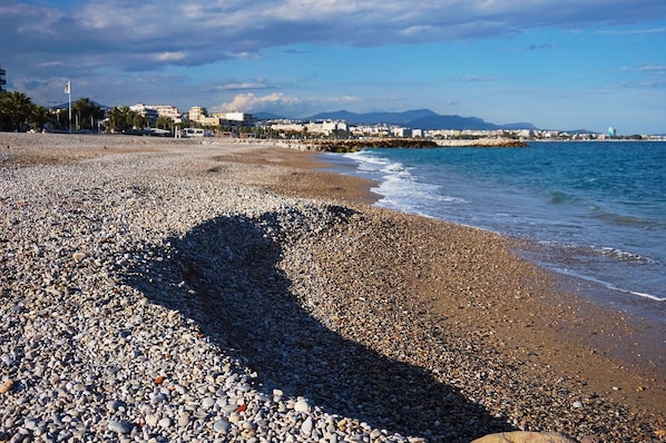 A pebble beach with a clear view of the sea and distant buildings. - Room with Private Bathroom and Air Conditioning – Cagnes-sur-Mer (Cagnes-sur-Mer)