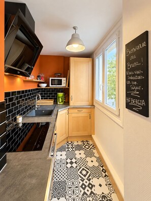 A modern kitchen with black and white patterned tiles, a microwave, and a chalkboard with a welcome message. - New Listing (Chartres)