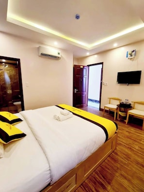 Een hotelkamer met een bed, een airconditioning, een televisie en een eettafeltje met stoelen.