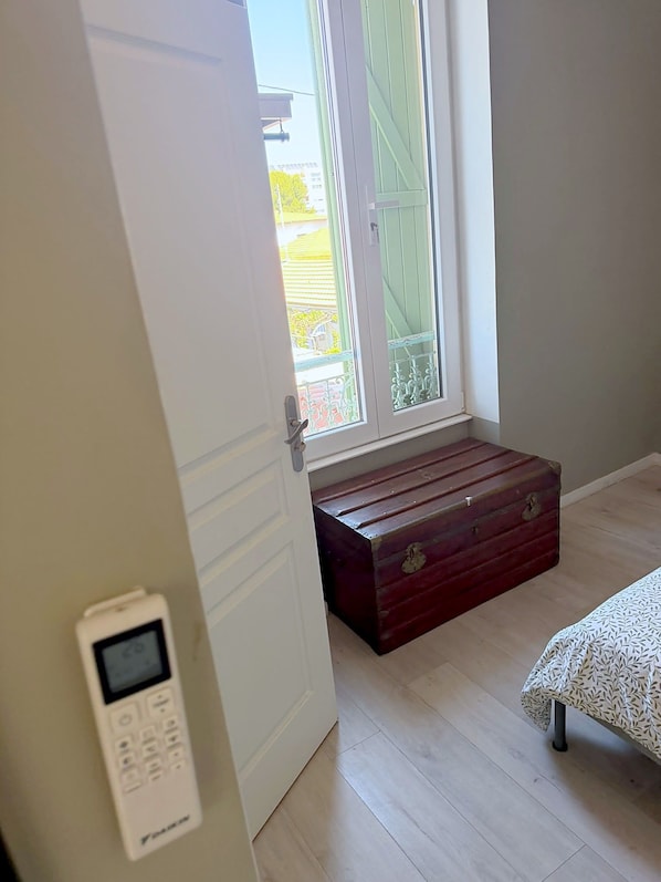 A room with a wooden bench, a white door, and a window with a view of buildings. - Room with Private Bathroom and Air Conditioning – Cagnes-sur-Mer (Cagnes-sur-Mer)