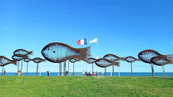 A coastal area with a series of metal sculptures resembling fish, a flagpole with a flag, and a clear view of the sea.