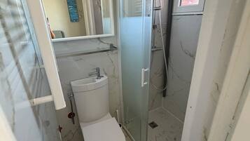 Kylpyhuone, jossa on wc, pesuallas ja lasinen suihkuseinä.