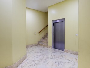 Un pasillo con piso de mármol, una escalera y una puerta cerrada de ascensor.