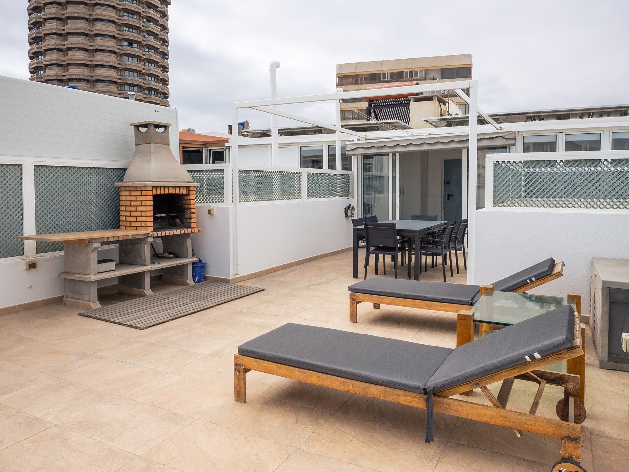 Una terraza en la azotea con zona de barbacoa, asientos y vistas a la ciudad.