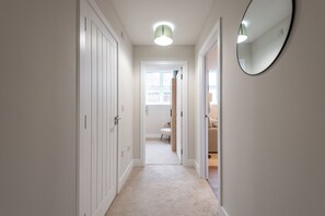 A narrow hallway with white doors, a carpeted floor, and a mirror on the right wall. - Modern 1BR Flat in Historic Hull Old Town (Kingston upon Hull)