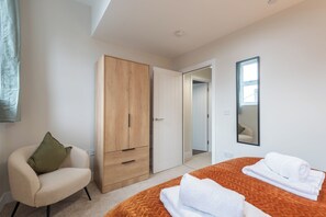 A bedroom with a bed, a wardrobe, a chair, a mirror, and a door leading to another room. - Modern 1BR Flat in Historic Hull Old Town (Kingston upon Hull)