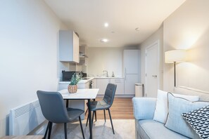 A modern kitchen with white cabinets, a dining table with chairs, and a sofa with cushions. - Modern 1BR Flat in Historic Hull Old Town (Kingston upon Hull)