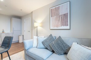 Ein modernes Wohnzimmer mit einem grauen Sofa, einer Stehlampe und einem großen abstrakten Gemälde an der Wand.