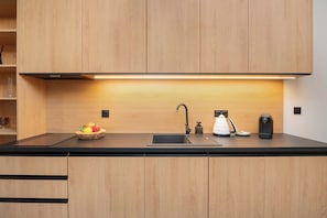 Una cucina moderna con un piano di lavoro nero, mobili in legno, un lavello incassato, un bollitore, una macchina da caffè e una ciotola di frutta.