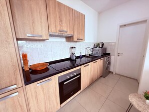 A modern kitchen with wooden cabinets, a black countertop, a built-in oven, and a washing machine. - East Legon 1BR·2 Balconies·Pool·Gym·Backup Power (Accra)