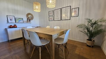 Un comedor con una mesa de madera, cuatro sillas, una planta en maceta y cuadros en la pared.