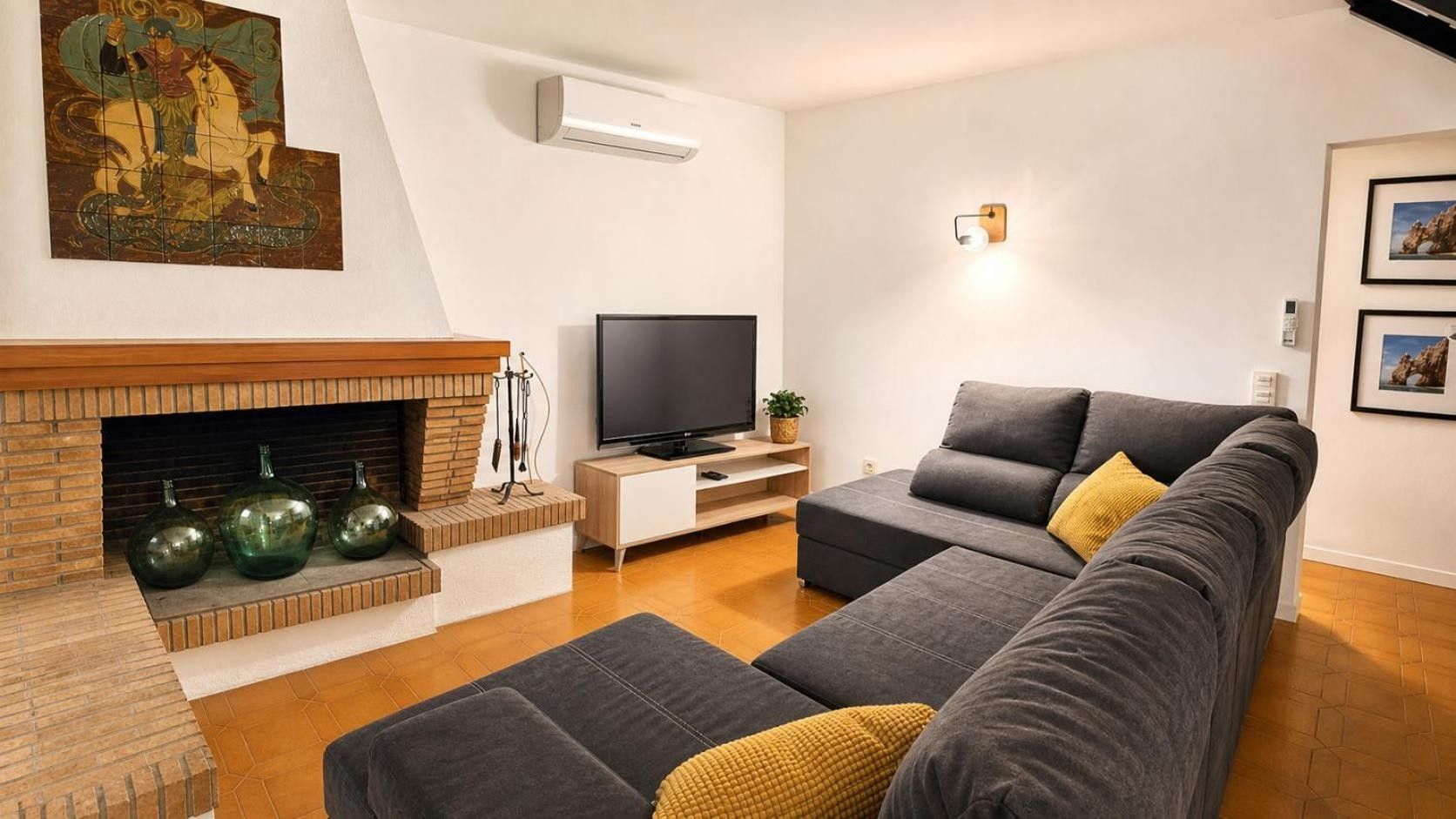 Ein modernes Wohnzimmer mit Kamin, Flachbildfernseher und grauem Sofa mit Kissen.