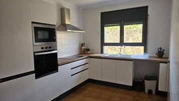 Una cocina con armarios blancos, un horno negro, un microondas, un ventanal con vistas y un fregadero.