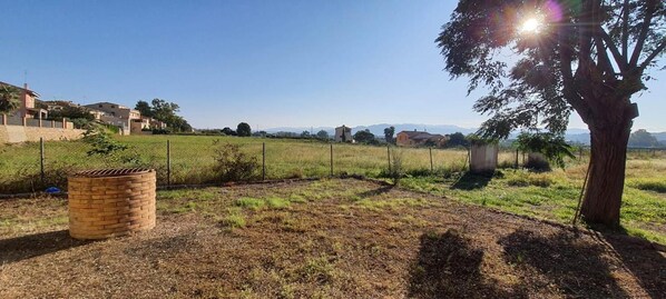 A fenced outdoor area with a brick structure, a tree, and a clear view of distant buildings. - Country House 'La Sènia' with Mountain View, Wi-Fi and Air Conditioning (Miravet)