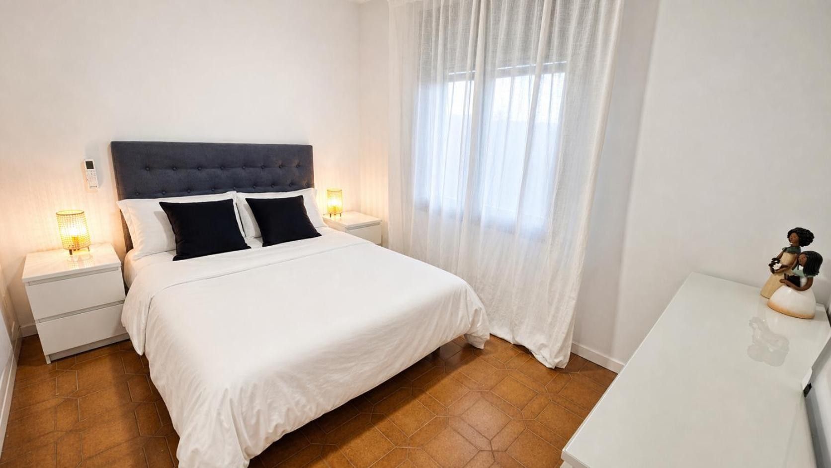 Ein Schlafzimmer mit einem Bett, Nachttischen, einem Beistelltisch und einem Fenster mit Vorhängen.