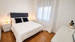 A bedroom with a bed, nightstands, a bedside table, and a window with curtains. - Country House 'La Sènia' with Mountain View, Wi-Fi and Air Conditioning (Miravet)