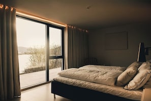A bedroom with a large window, a bed, and a chair.
