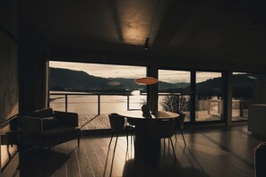 A modern interior with a large window overlooking a body of water and hills.