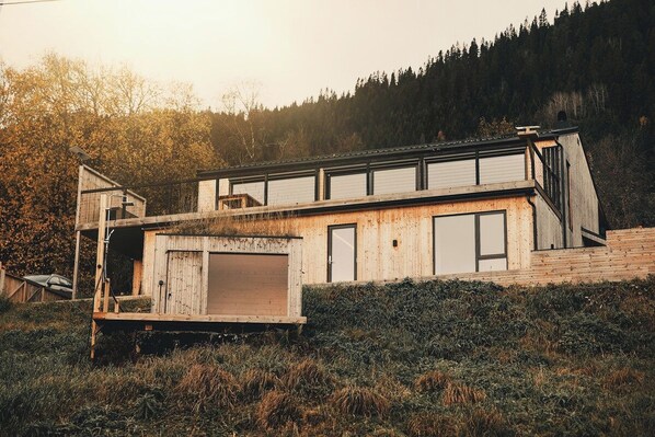 A modern house with a sloped roof, a wooden deck, and a large window.