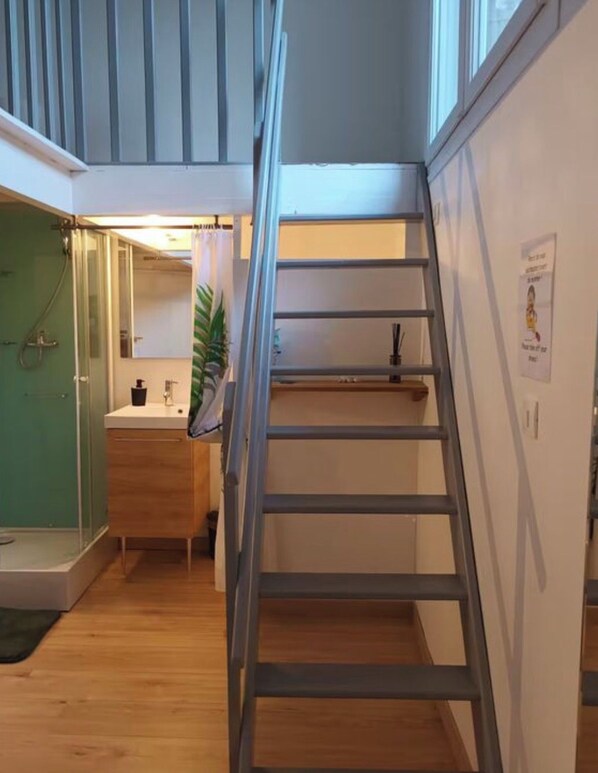 Un escalier en bois avec une rampe métallique menant à un espace situé au deuxième étage, qui comprend une fenêtre et une porte.