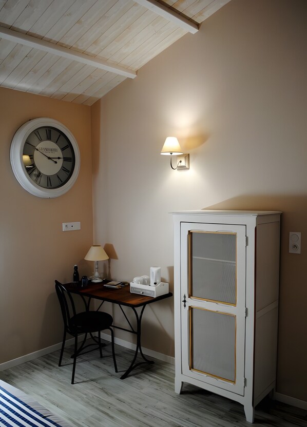 A room with a wooden ceiling, a round wall clock, a table with a lamp, a cabinet, and a wall-mounted light fixture.