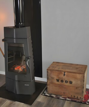 A wood-burning stove with a glass door, a wooden box labeled 'WOOD 1944', and a black vertical object to the right.