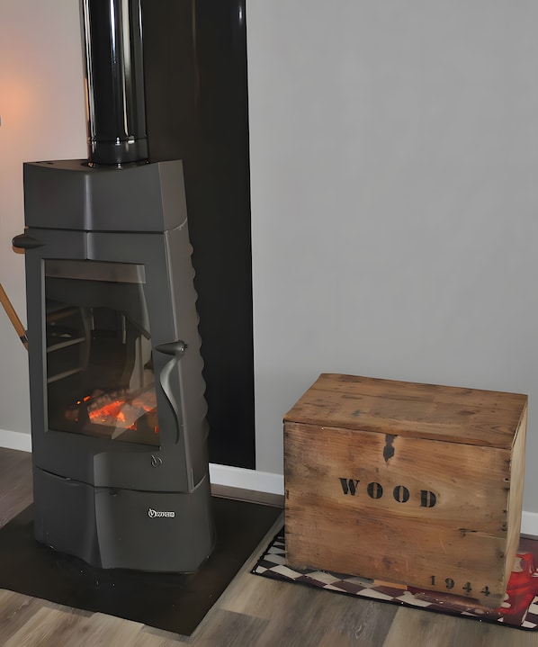 A wood-burning stove with a glass door, a wooden box labeled 'WOOD 1944', and a black vertical object to the right.