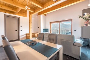Una stanza con un tavolo da pranzo, sedie, un divano, una TV e una finestra vista montagna.
